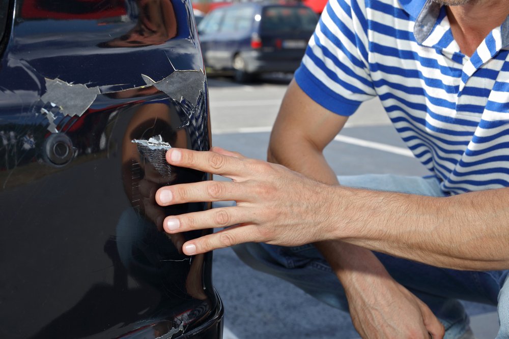 Un hombre señalando los daños causados por un accidente en el estacionamiento.