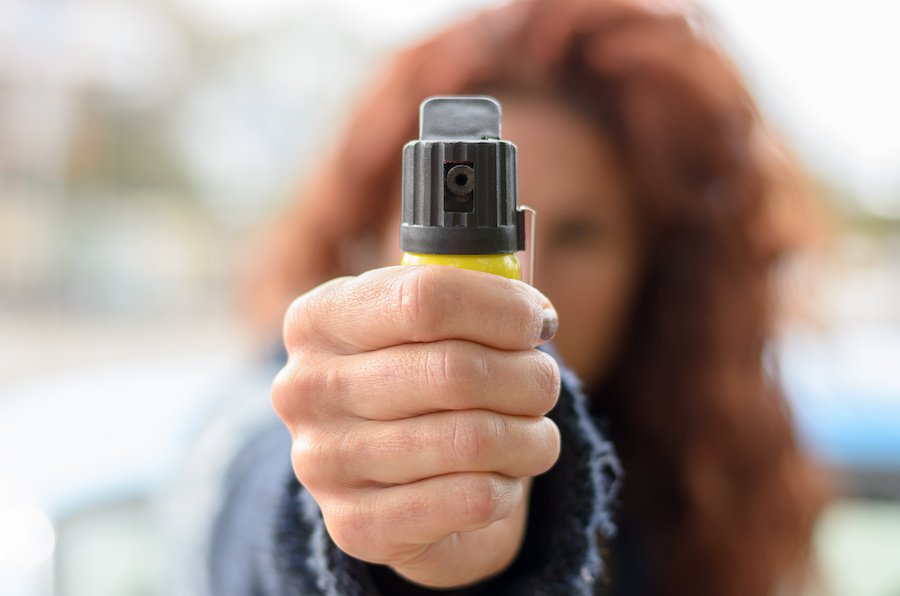 Close up of pepper spray in hand of partially obscured red haired woman standing outside