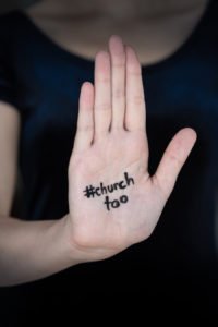 Woman's open hand held out with "#churchtoo" written on palm to protest sexual abuse in the church