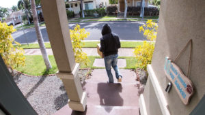 Ladrón de paquetes captado en el sistema de video portero robando una caja de entrega en la escalera de una casa suburbana