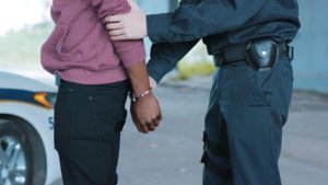 ICE officer arresting immigrant by police car