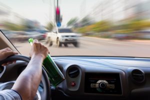 Imagen borrosa de un conductor sosteniendo una botella de cerveza manejando hacia el tráfico