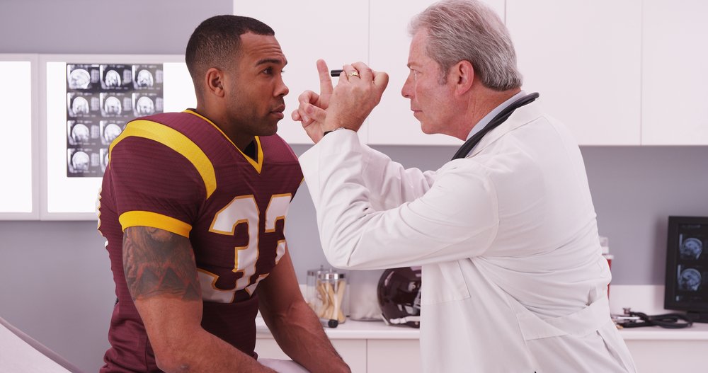 A man in a football uniform being checked out by a neurologist after he received a concussion.