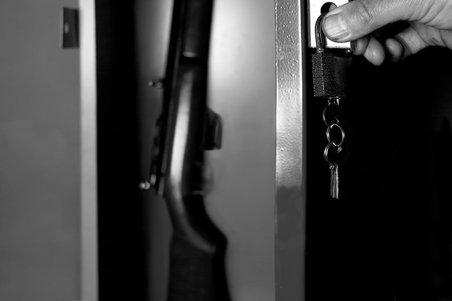 Foto en blanco y negro de una mano humana abriendo un gabinete de armas que sostiene un rifle