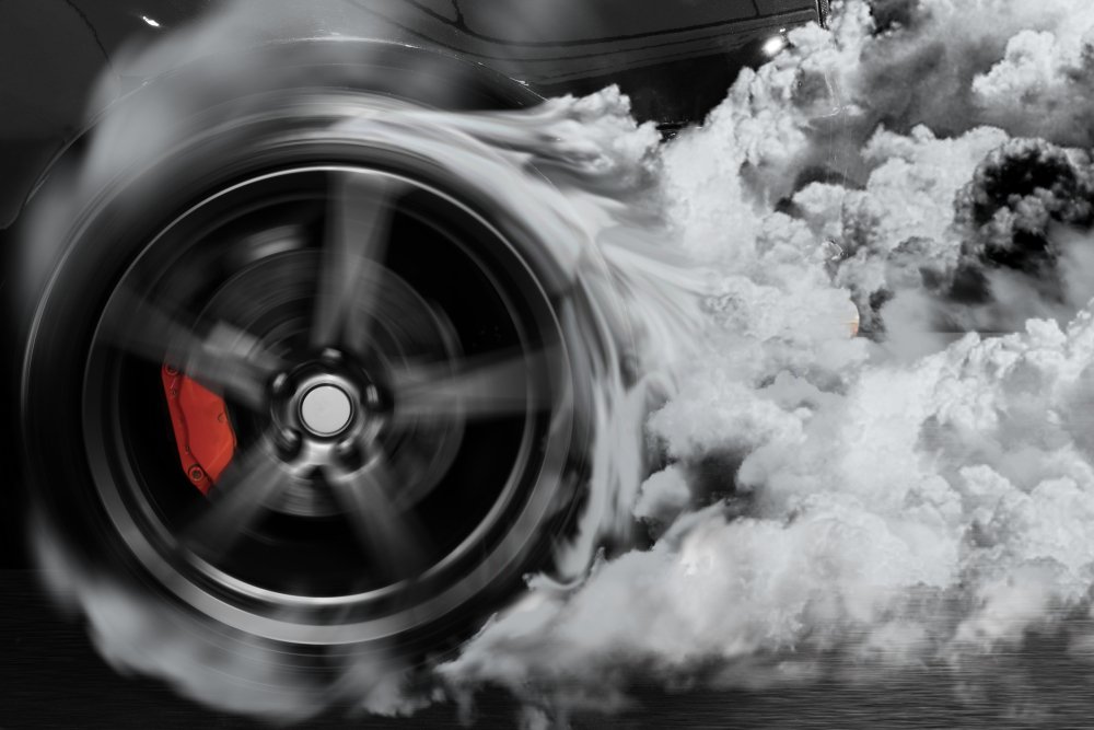 A smoking tire most likely making a squealing sound as it spins quickly.