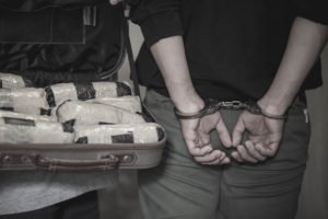 Man in handcuffs next to case of heroin in packs