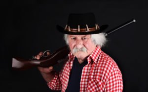 Menacing-looking bounty hunger slinging a rifle over his shoulder against a black background