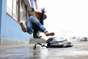 A young man slipping and falling on a seemingly slippery sidewalk.