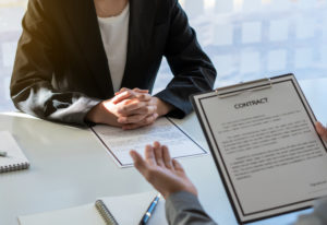 Empleador discutiendo el contrato de empleo con un nuevo empleado. Están sentados uno frente al otro en el escritorio del empleador.