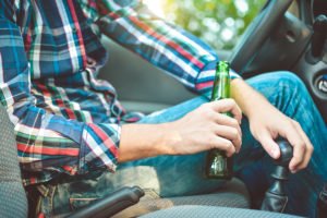 Drunk young man driving a car with a bottle of beer.