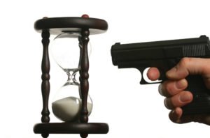 A gun pointed at an hourglass, representing the time left in a possible statute of limitations.