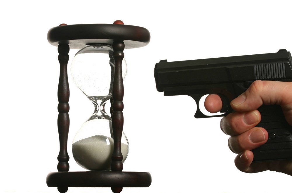 A gun pointed at an hourglass, representing the time left in a possible statute of limitations.