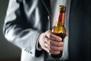 A suited man, possibly a candidate for a federal job, holding a beer.