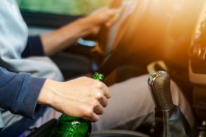 Hombre conduciendo con una mano en el volante y la otra sosteniendo una botella de cerveza