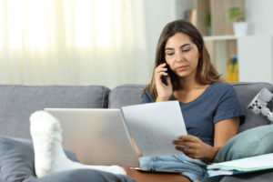 A woman with cast on her foot on the phone trying to negotiate her medical bills after she received her personal injury settlement.