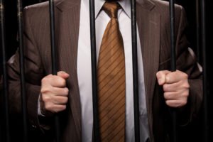 Closeup of a man in a business suit gripping prison bars