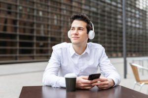 An office worker sitting outside during his break listening to music and having a coffee.