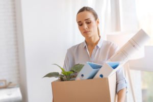 A dejected office worker holding a box filled with her belongings as she leaves the office where she was possibly wrongfully terminated from.