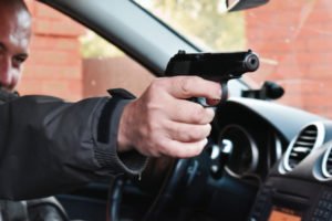 Hombre apuntando con un arma desde un vehículo