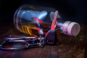 A bottle of whiskey next to car keys and handcuffs, suggesting at a potential DUI arrest and possibly a bail hearing.