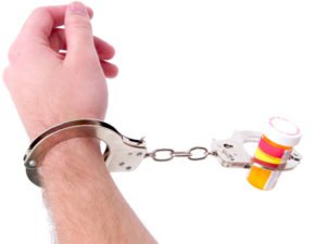 handcuffs holding a hand and a bottle of pills