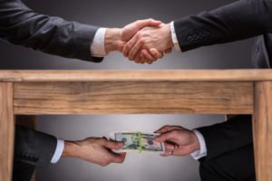 Manos que se estrechan sobre la mesa con otras manos intercambiando dinero debajo de la mesa