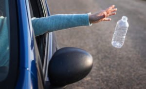 Hand throwing out plastic water bottle from moving car