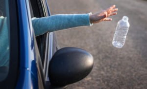 Mano arrojando botella de agua de plástico desde un coche en movimiento