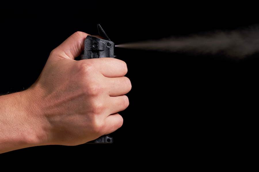 Closeup of hand on pepper spray cartridge against black background