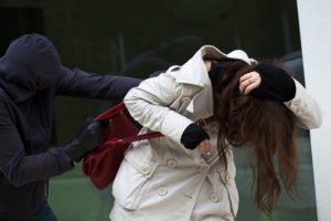 A hooded robber grabbing a woman's purse and trying to run away with it.