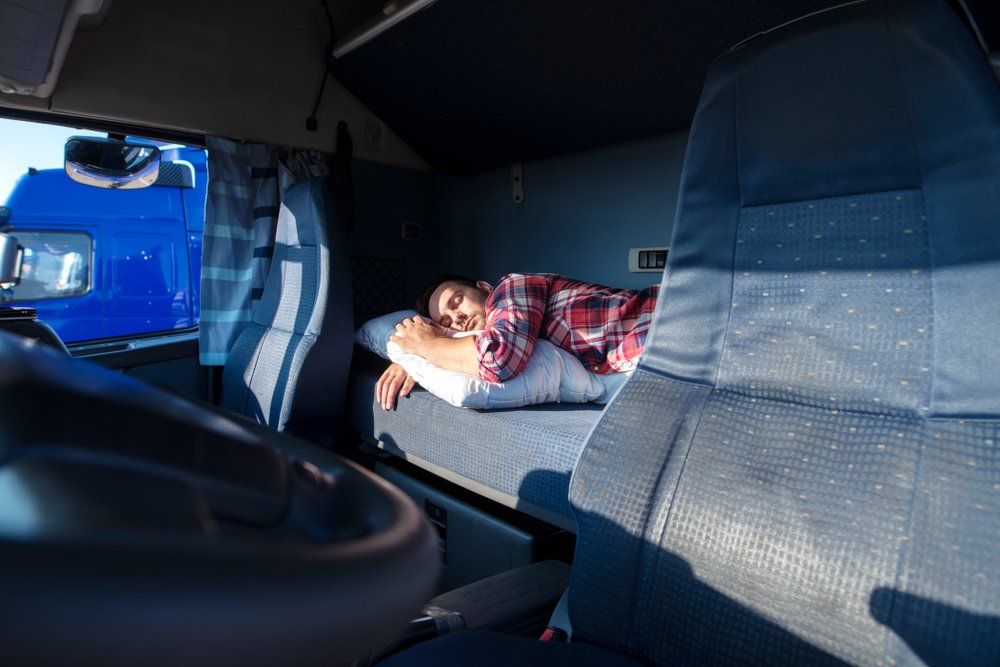 A truck driver sleeping in the sleeping cabin of his truck.