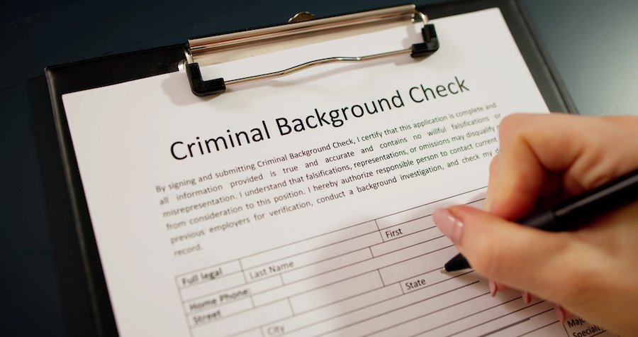 Clipboard with a paper that says "Criminal background check," and a hand is filling it out with a pen
