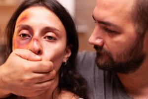 Mujer con un ojo morado con su esposo abusivo sosteniendo su boca