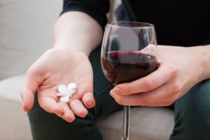 A man holding pills in one hand and a glass of wine in the other, possibly leading to a DUI if he drives while intoxicated.