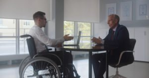 A disabled man in a wheelchair, speaking with his workplace superior about harassment.