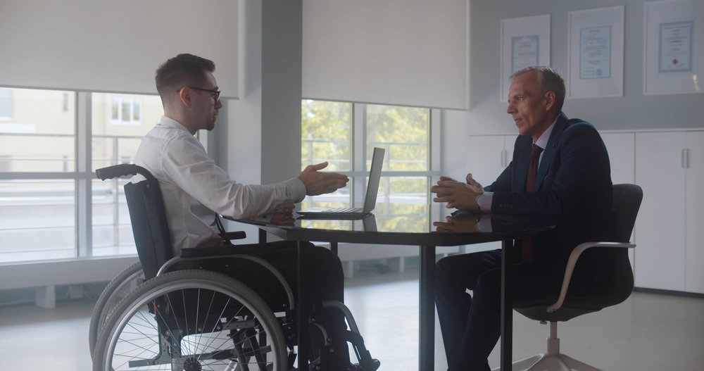 A disabled man in a wheelchair, speaking with his workplace superior about harassment.