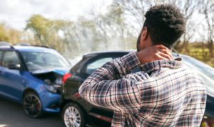 A man rubbing his neck after a car accident, where the other person possibly does not have insurance, further complicating his situation.