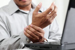 Man holding his wrist in pain while behind computer