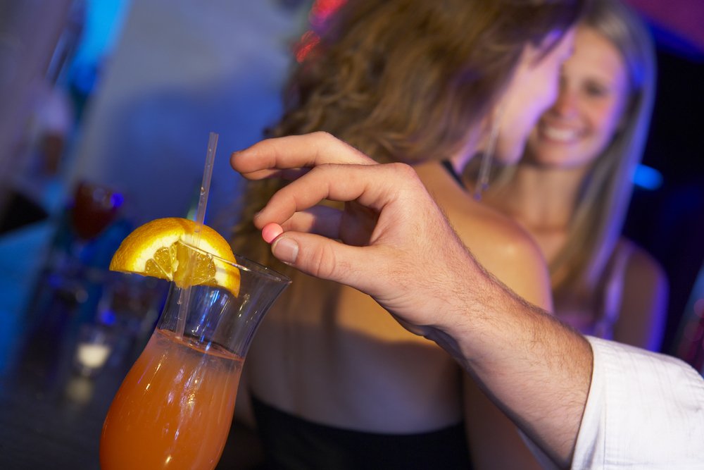 A man dropping a pill into a drink, possibly leading to involuntary intoxication.