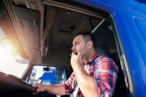 A tired truck driver yawning while he is behind the wheel.