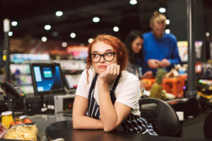 A retail worker bored due to the lack of activity at work. Her manager may possibly ask her to take the rest of the day off since there is so little work to do.