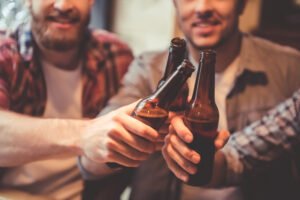 A group of friends clinking their beers prior to drinking them. Hopefully they will be careful not to drink too many or else they might get a DUI.