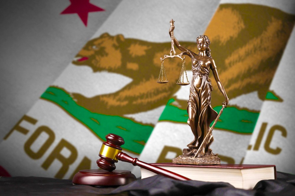 Una estatua de Lady Justice frente a la bandera del estado de California.