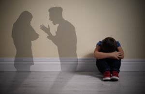 Silhouette of fighting parents with child crouching by wall
