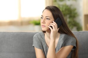 A woman about to call her insurance provider about her recent DUI, possibly having second thoughts.