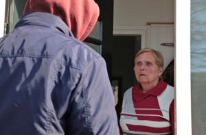 Older woman looks scared at a suspicious person at the door