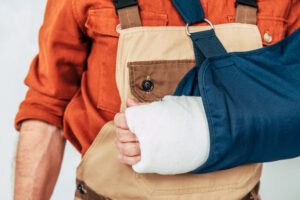 A construction worker's arm is covered by an arm cast and supported by a sleeve. His injury may potentially be covered under workers' comp.