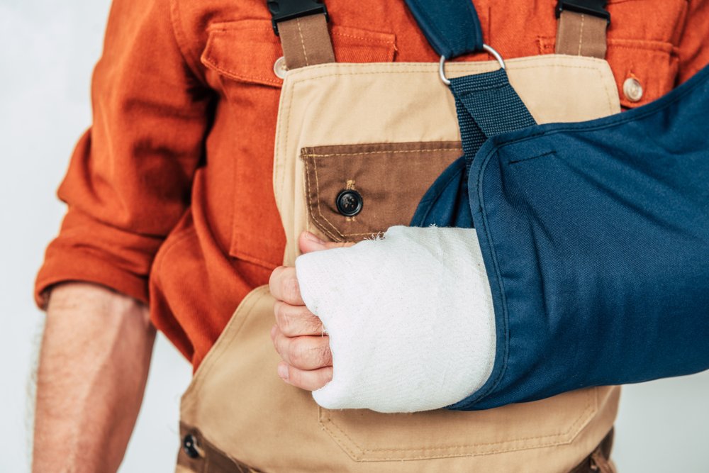 A construction worker's arm is covered by an arm cast and supported by a sleeve. His injury may potentially be covered under workers' comp.
