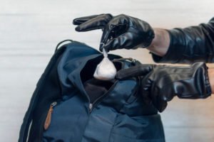 Manos con guantes plantando drogas en una mochila