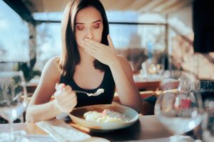 Mujer enfermándose mientras come un tazón de fideos en un restaurante